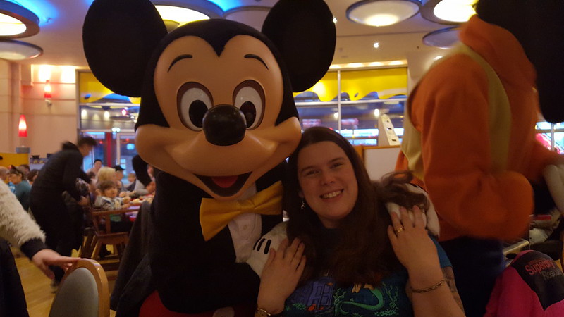 Woman sitting at a table with Mickey Mouse standing next to her