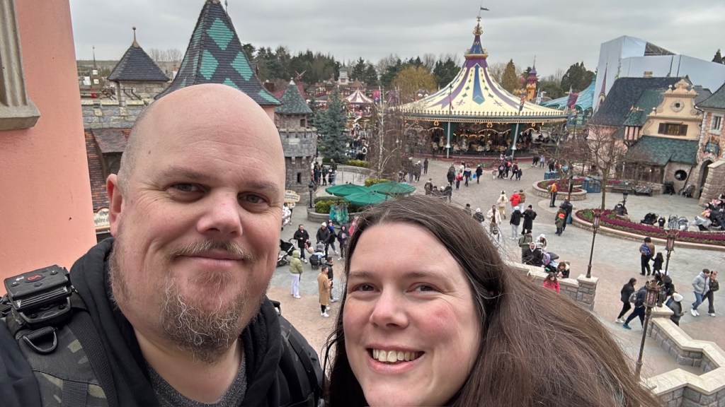Man and woman smiling at camera with Fantasyland in Disneyland Paris behind them