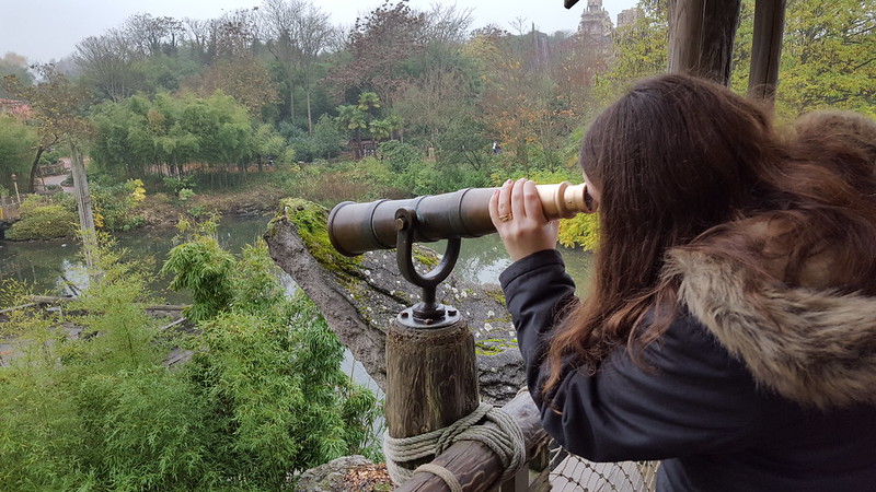 Woman looking through a telescope at greenery in Disneyland Paris