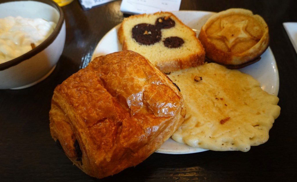 Pain au chocolate, pancake, cake slice and waffle on a plate.