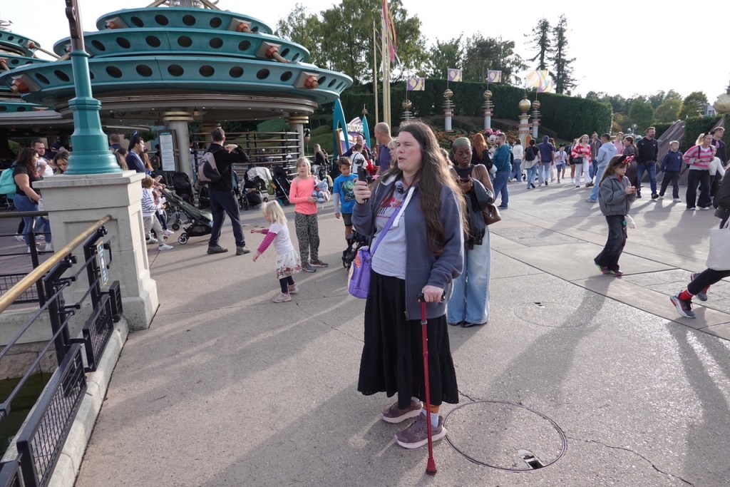 Woman holding a camera and walking stick filming in Discoveryland in Disneyland Paris