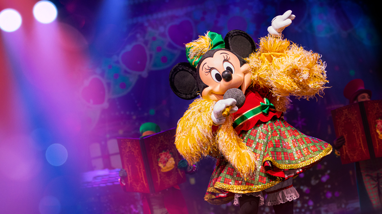 Minnie Mouse in a Christmas outfit and a microphone singing as part of Let's Sing Christmas! at Disneyland Paris